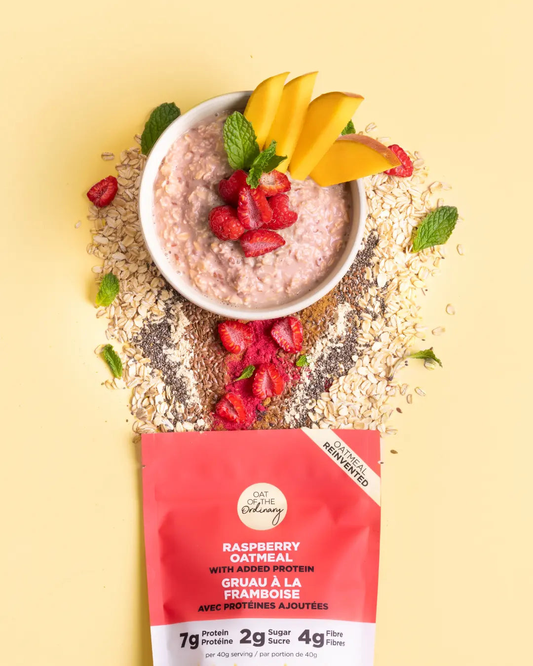 A bowl of raspberry protein oatmeal with mango and raspberry toppings and ingredients spilling out of a pouch.