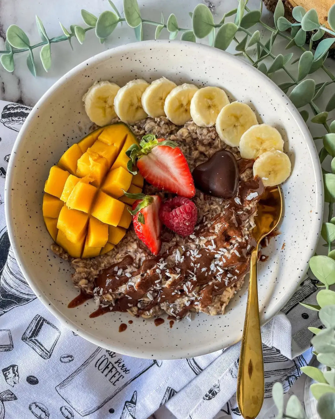 A bowl of chocolate oatmeal with mango, banana, and strawberry toppings.