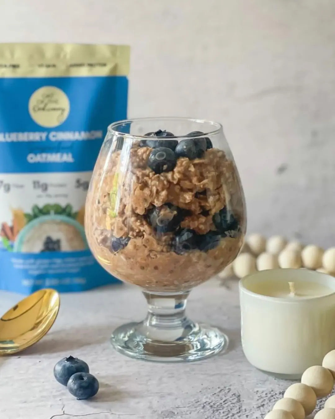 Blueberry oatmeal in a glass with a gold spoon and decorations.