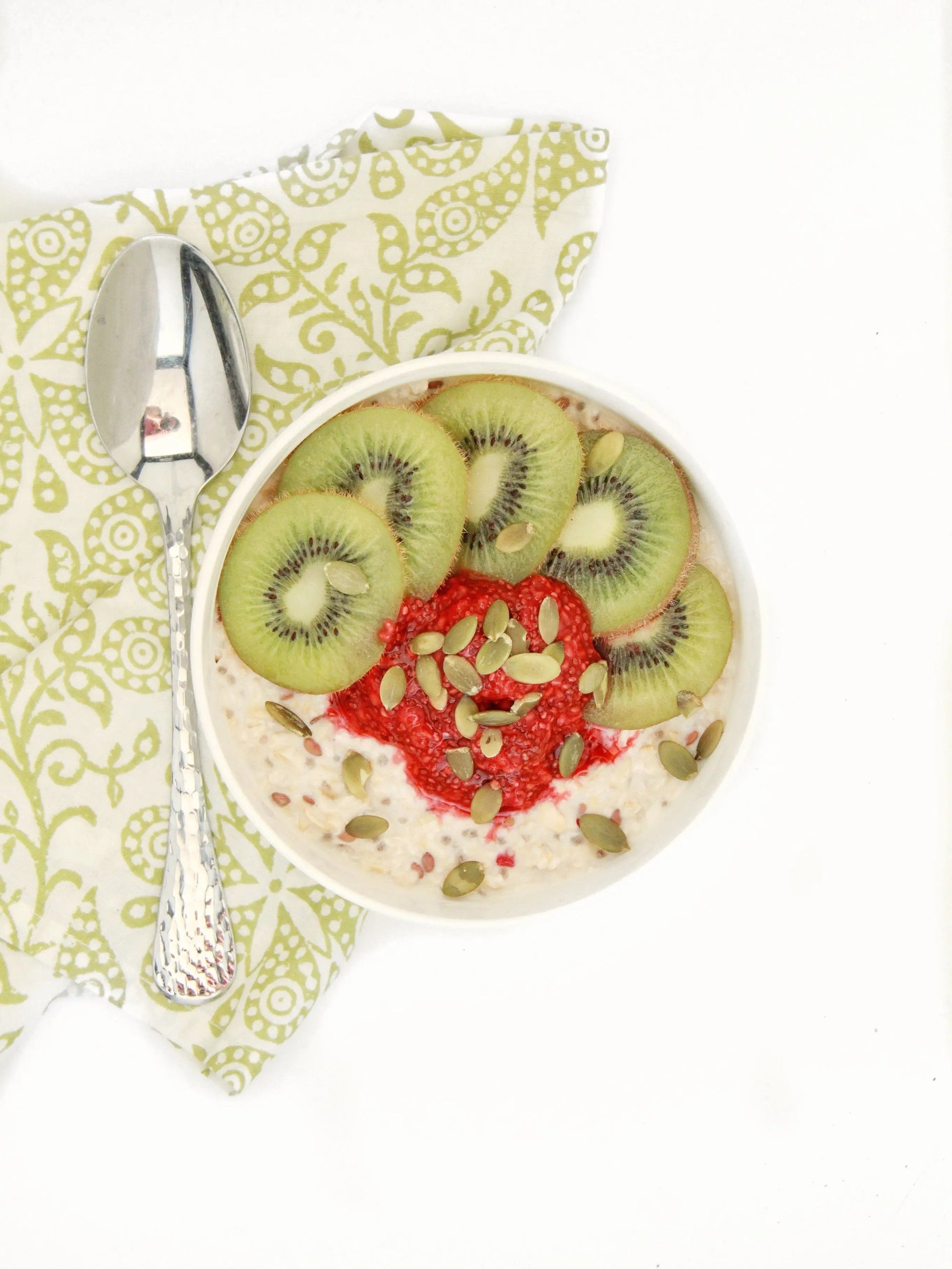 A decorative bowl of raspberry oatmeal with fresh kiwi toppings with pumpkin seeds and chia pudding.